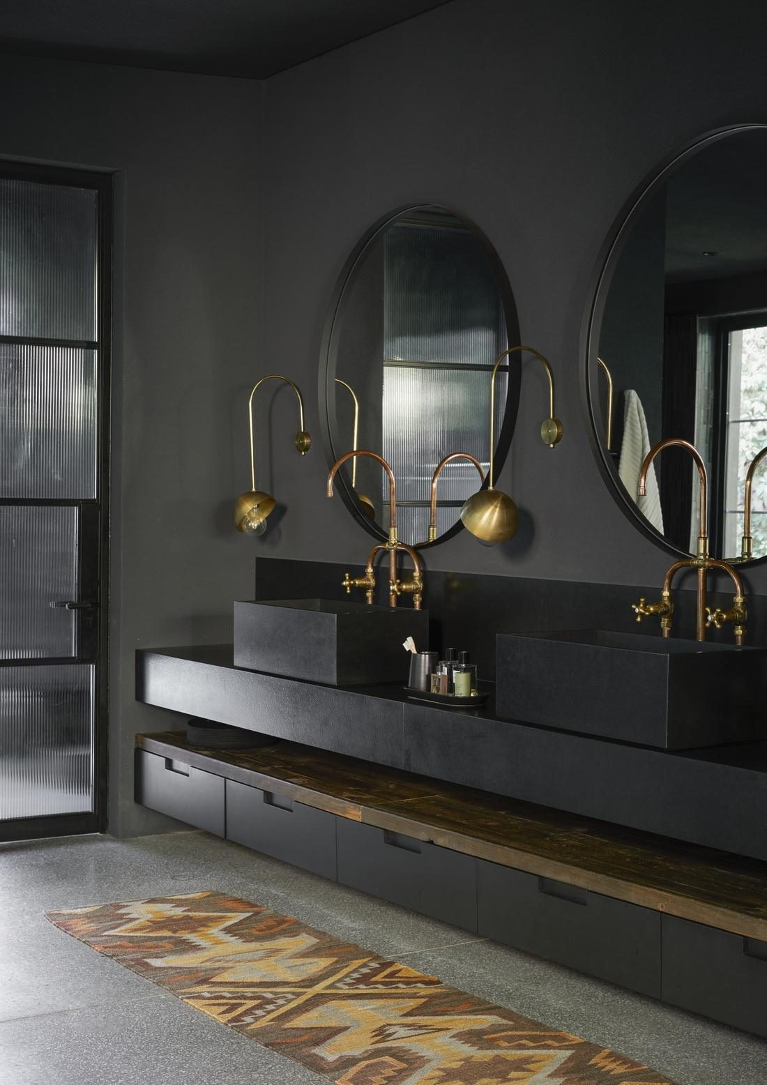 Bathroom with black stone basins, copper taps, round mirrors and brass wall lights