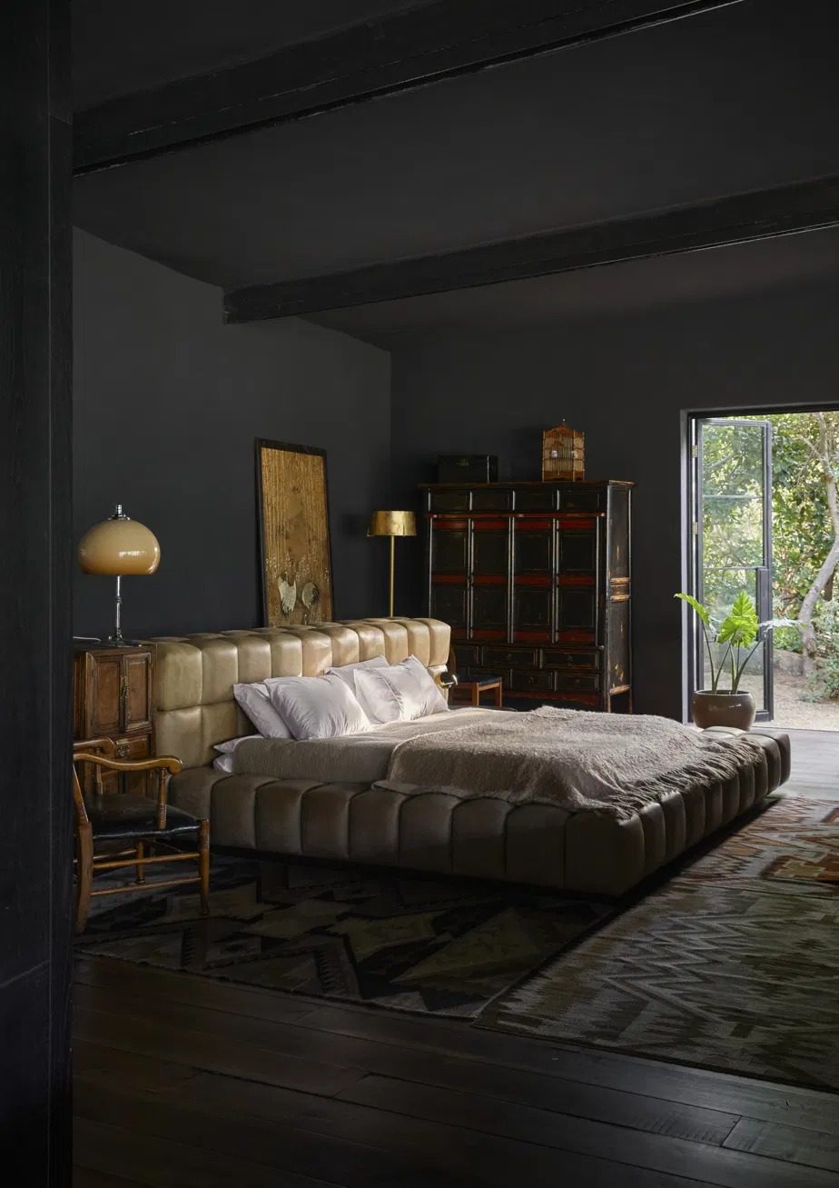 Bedroom with a low channel tufted leather bed, an antique lacquer cabinet and a door open to the garden