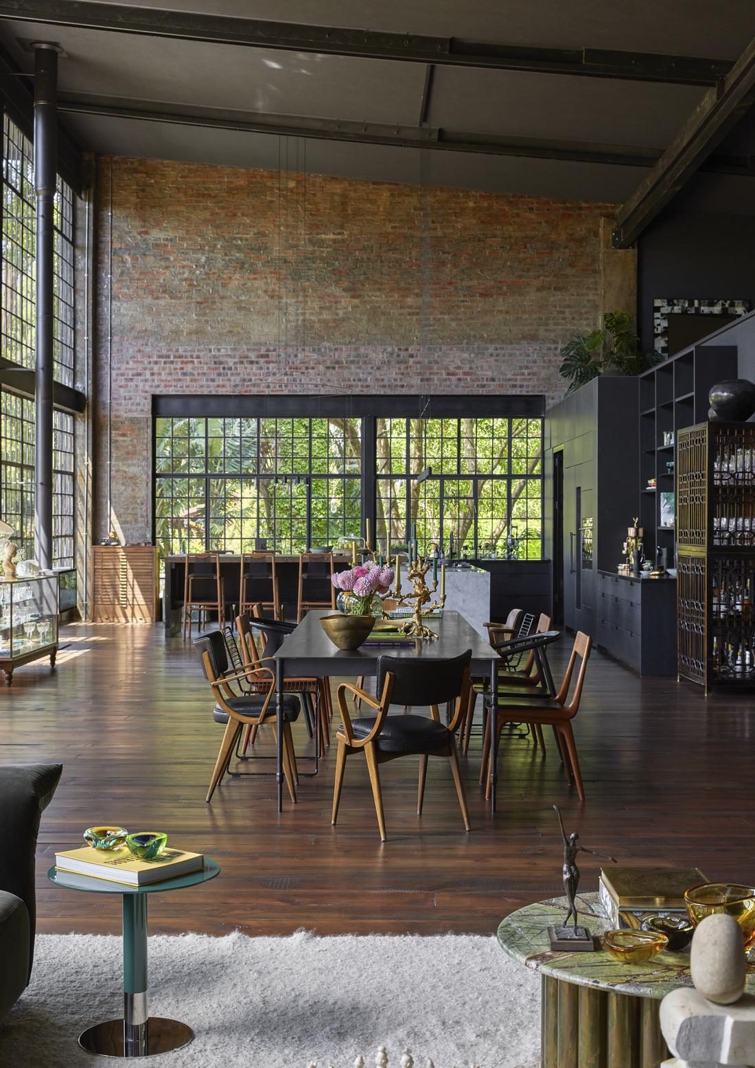Long dining table in the double height space, with a brick wall and garden views beyond