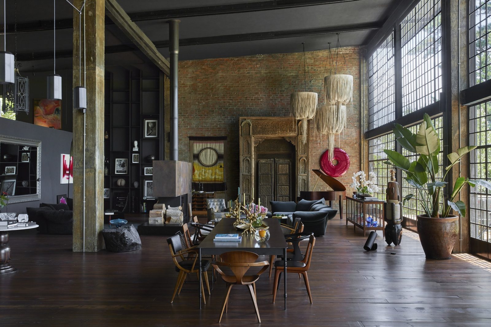 Wide view of the loft with a long dining table, green velvet sofas, a grand piano and a red glass sculpture on the brick wall