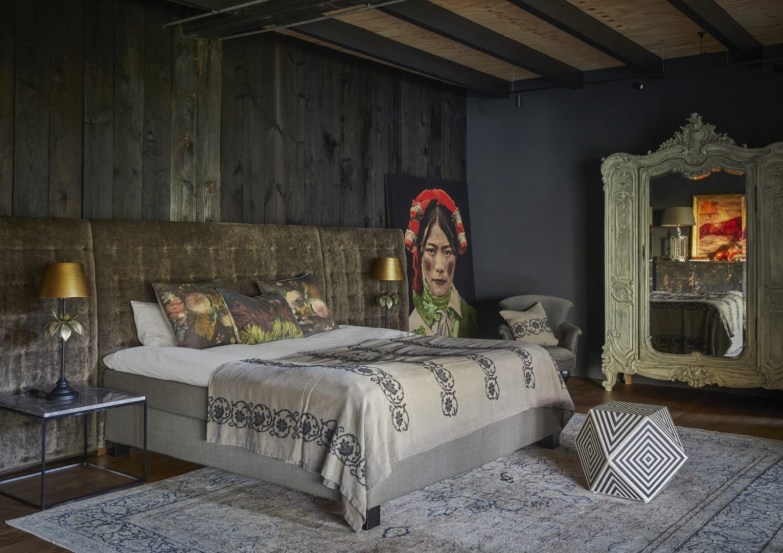 Bedroom with a tall velvet headboard, brass lamps, a portrait artwork and an ornate mirrored wardrobe